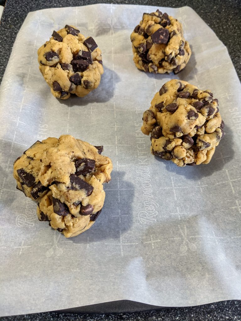 Four large chocolate chip cookie balls sitting on a parchment lined baking sheet.