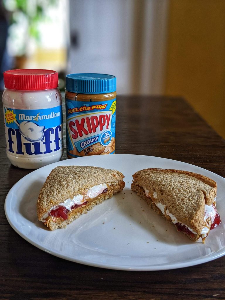 Cut in half fluffernutter sandwich on a white plate with a can of fluff and peanut butter in the background.