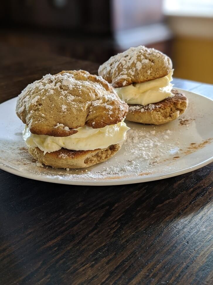 Two large snickerdoodle whoopee pies sitting on a white plate, doused with white powdered sugar.