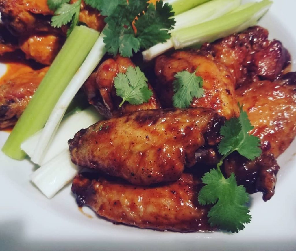 Glazed wings with celery on a white plate.