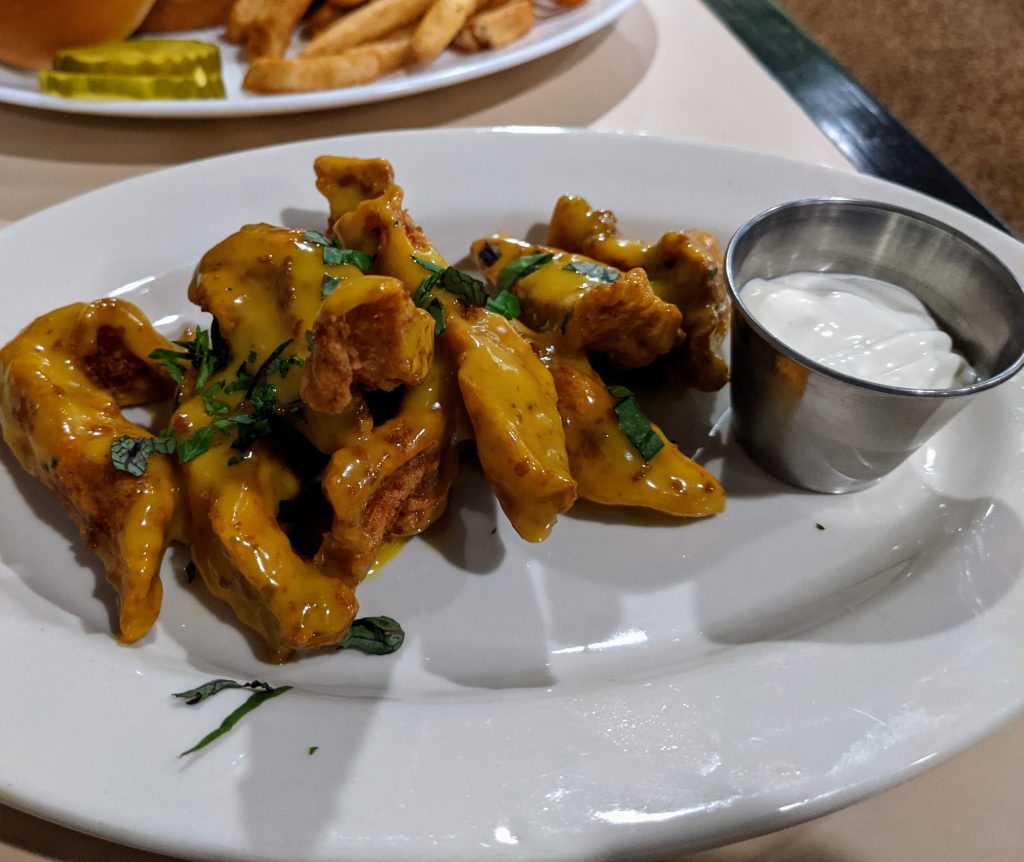 Honey mustard glazed wings with a white side sauce on a white plate.