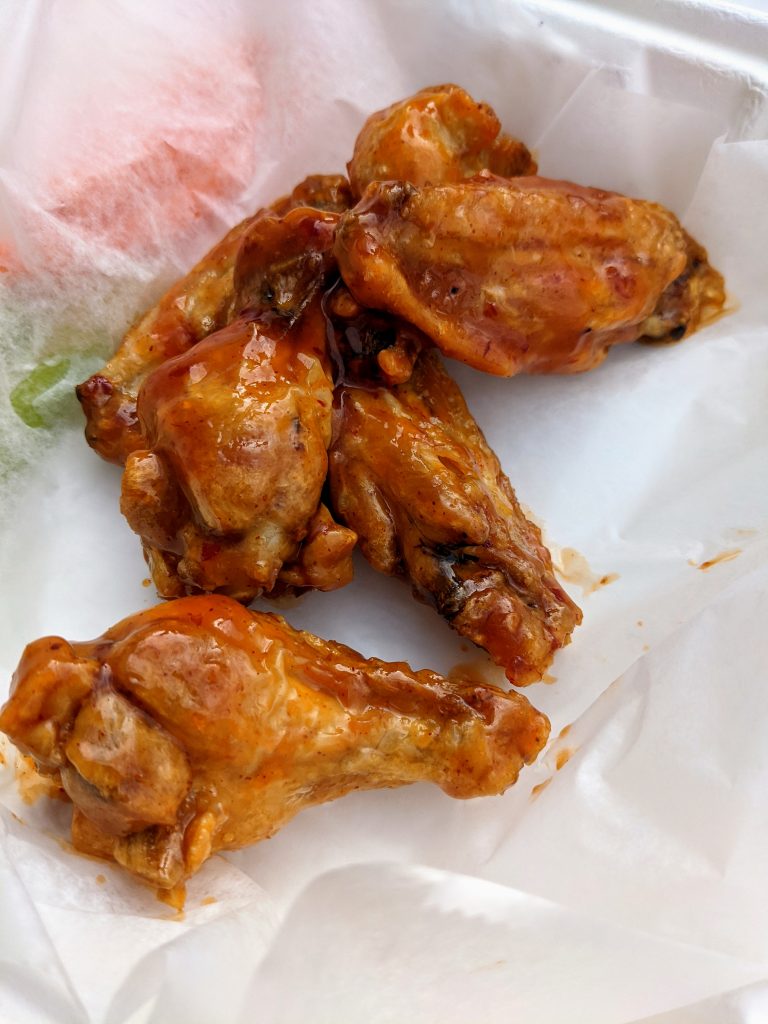 Honey BBQ sauce coated wings in a styrofoam container.