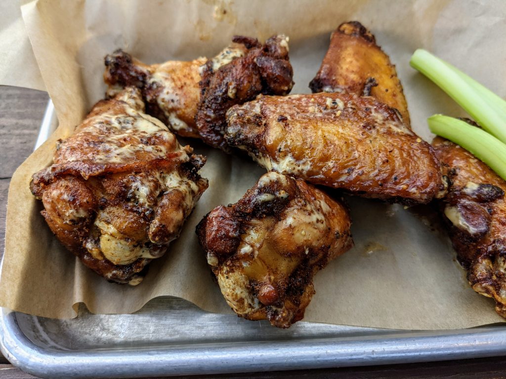 Wings coated with hints of a white-yellowish sauce and a side of celery on a metal tray.