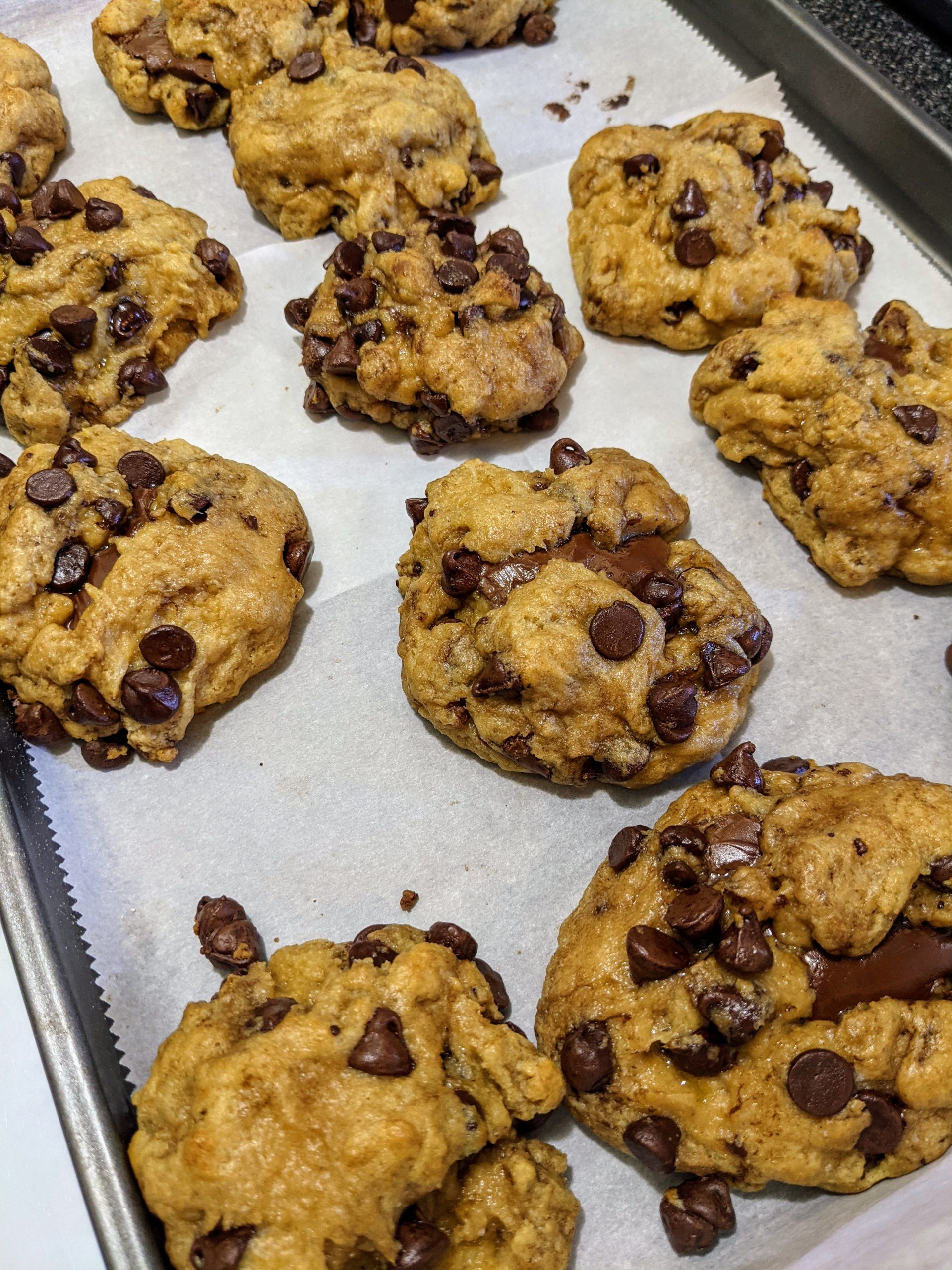 Several finished cookies filled with chocolate chips and Nutella fresh out of the oven sitting on a parchment lined baking sheet.