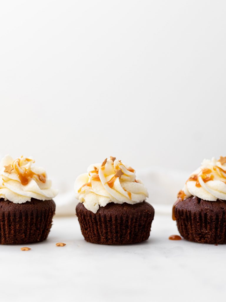 Three chocolate cupcakes with white frosting and light orange toppings sitting in a line next to each other.