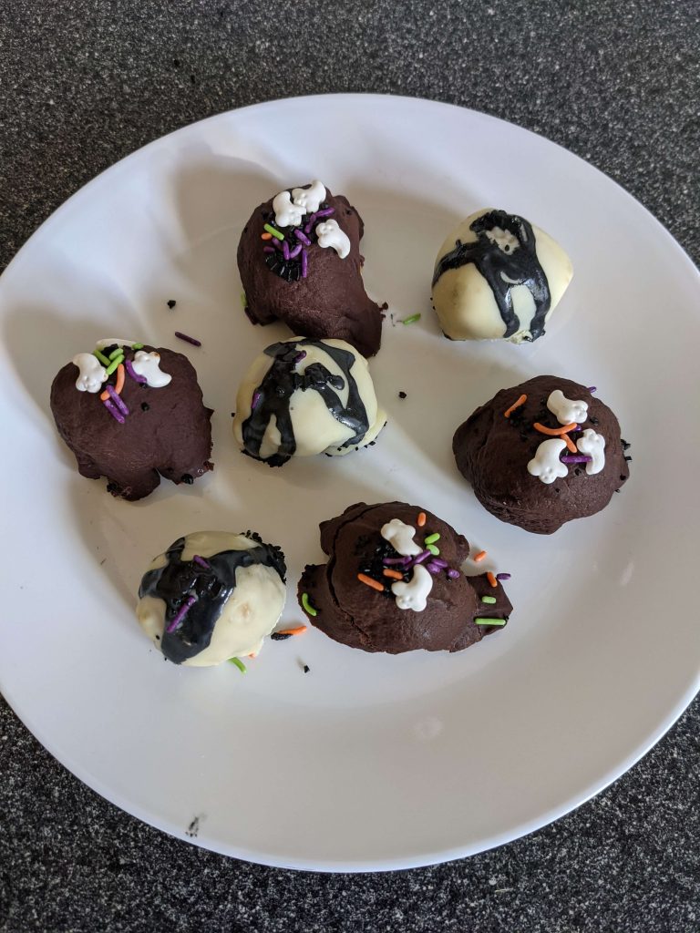 Several chocolate covered cookie balls on a white plate.