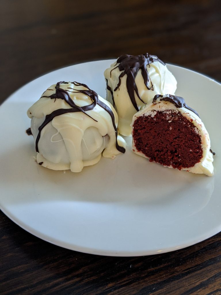 White chocolate covered red velvet cake balls on a white plate.