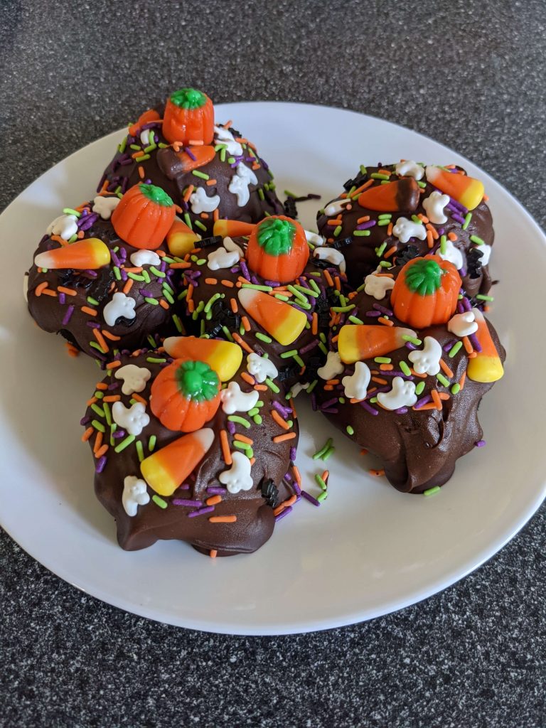Chocolate and Halloween sprinkle covered Oreo balls on a white plate.