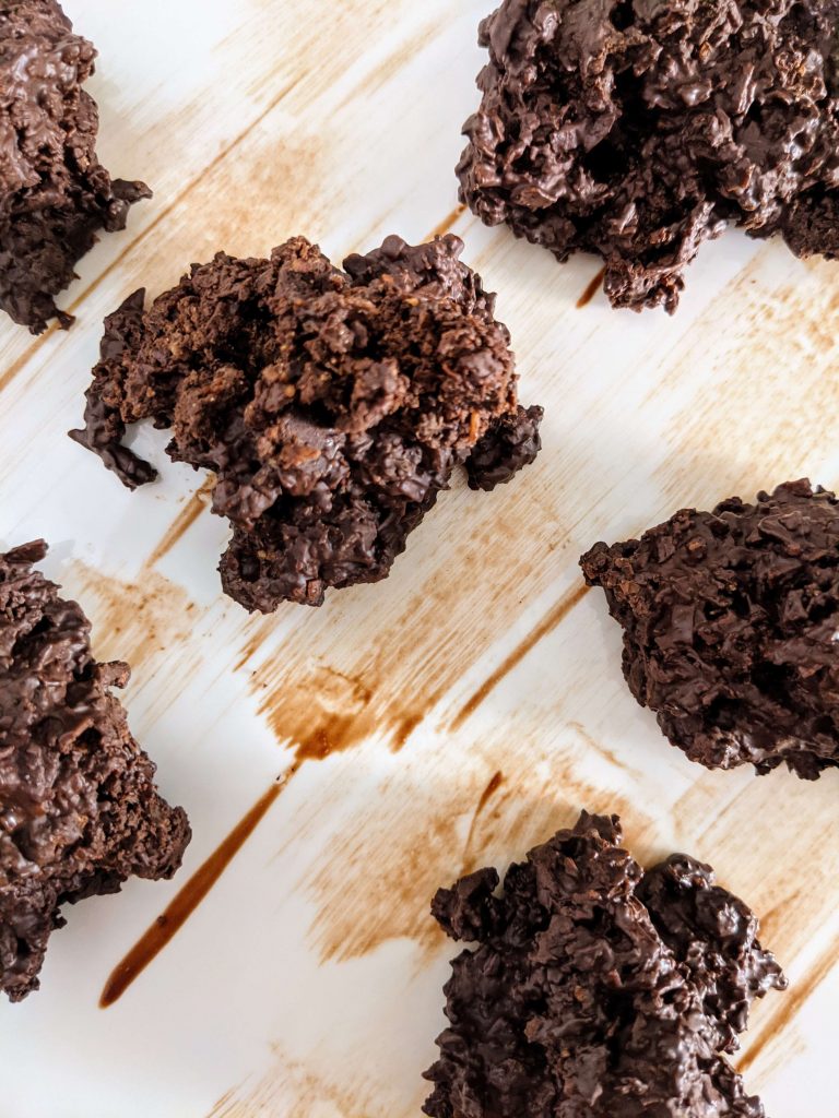 Several chocolate coconut haystacks sitting on top of a brown-white wooden board.