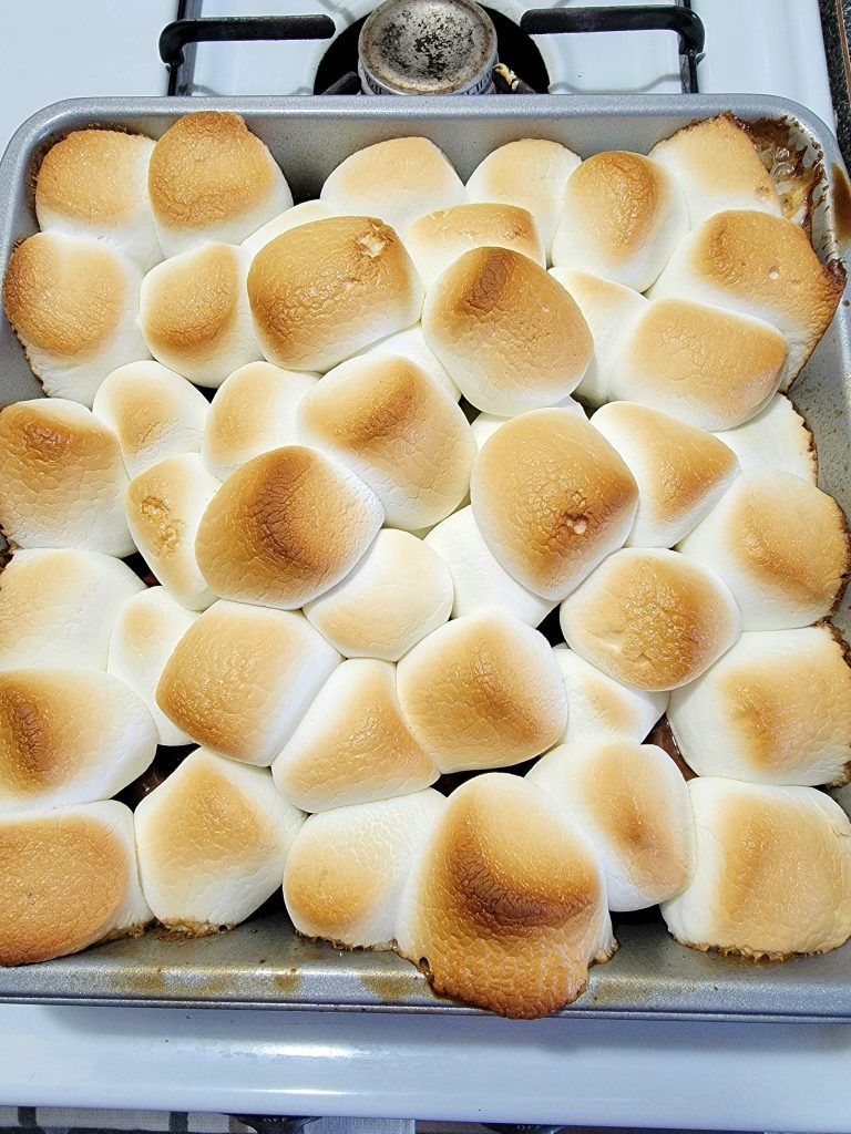 Finished baked smores with golden brown marshmallows on top sitting on stove in a baking pan.