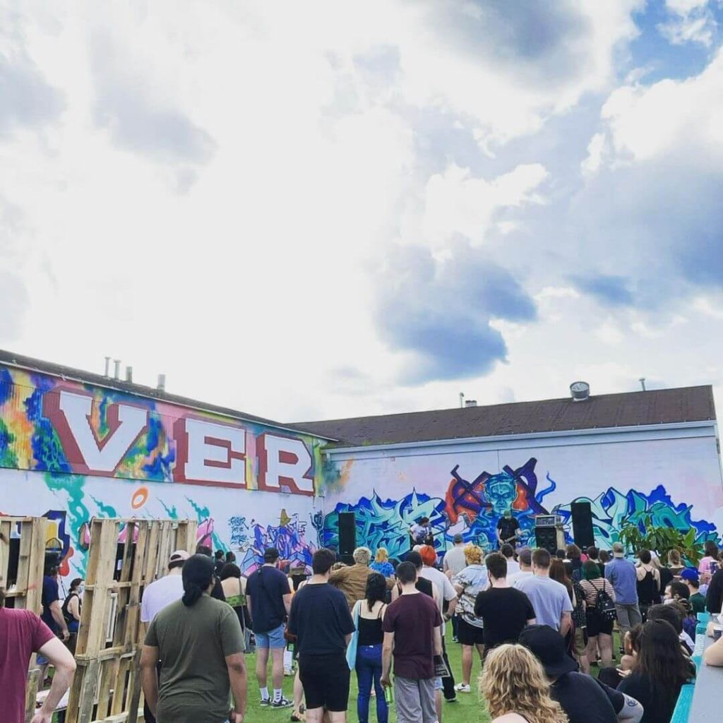 Outside with a large group of people at the side of a building.