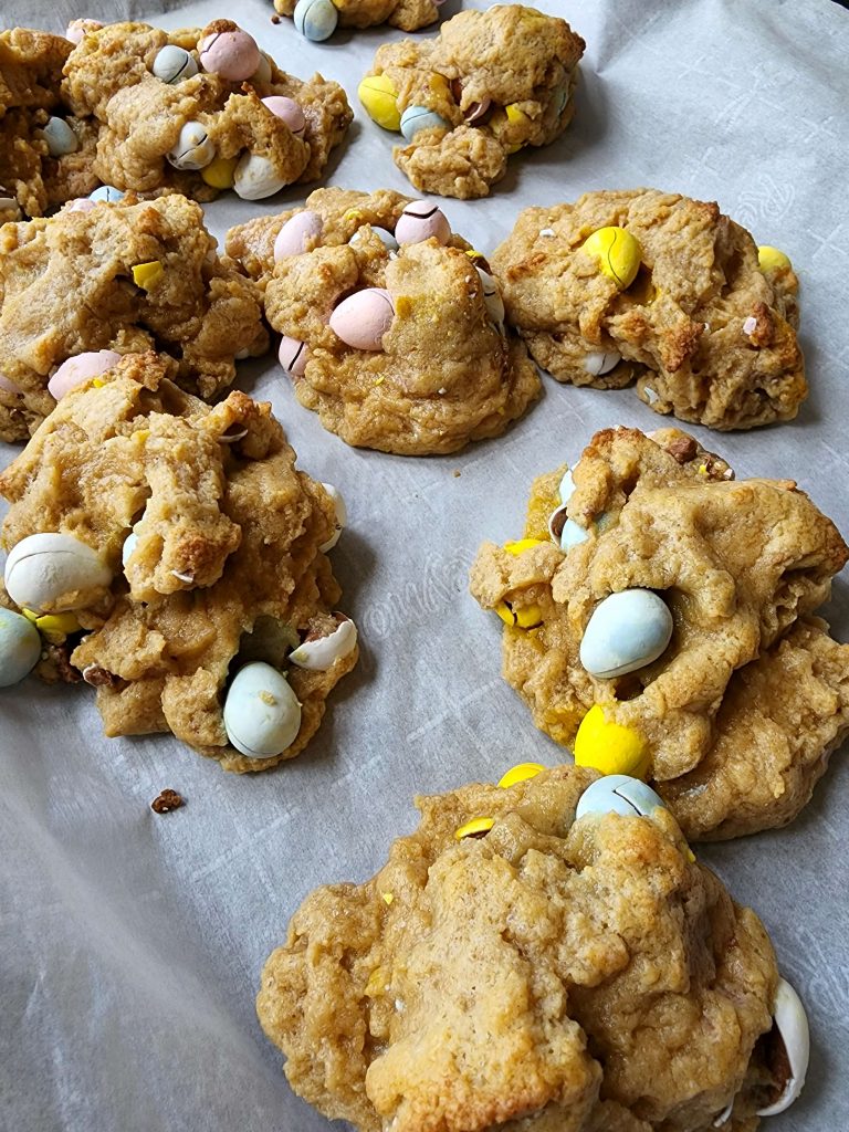 Side eye view of several large finished cookies with Easter egg chocolates inside them sitting on a parchment lined baking sheet.