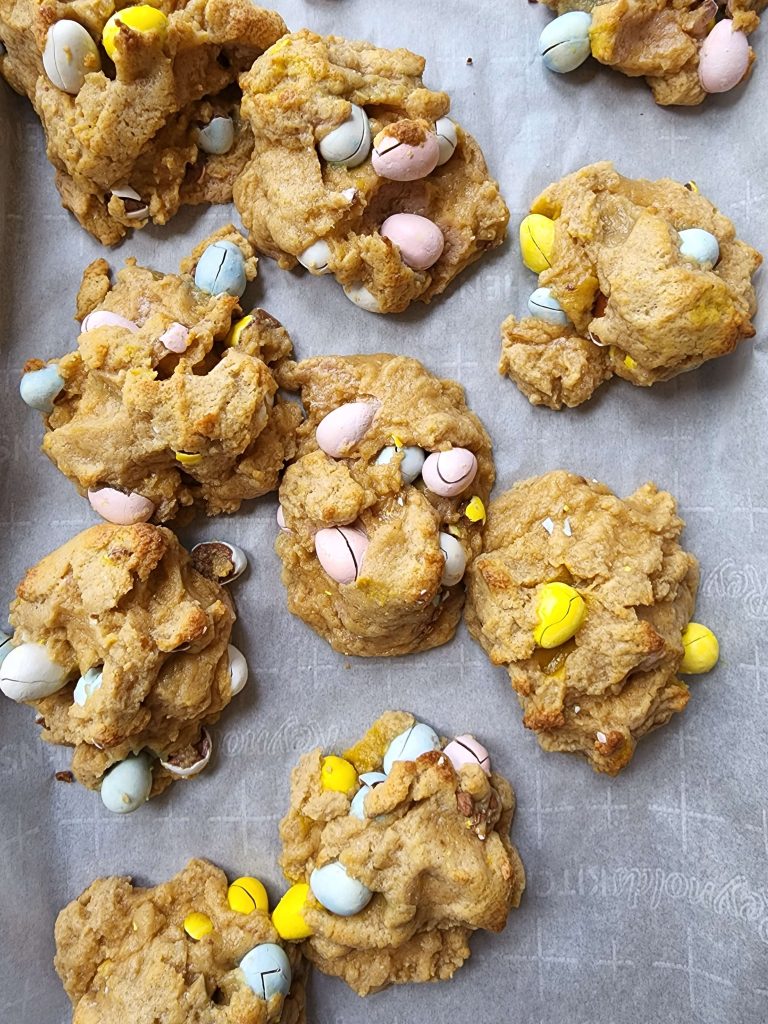 Birds eye view of several large finished cookies with Easter egg chocolates inside them sitting on a parchment lined baking sheet.