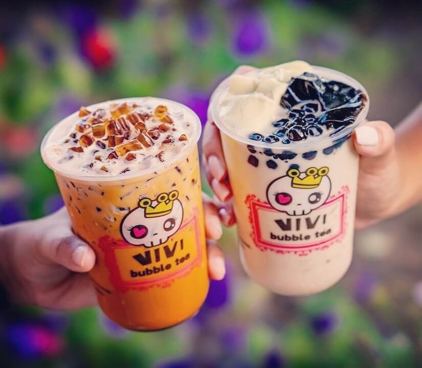 Two people with bubble teas "cheer." One tea is orange with toppings and the other is an orange-white with black boba toppings.