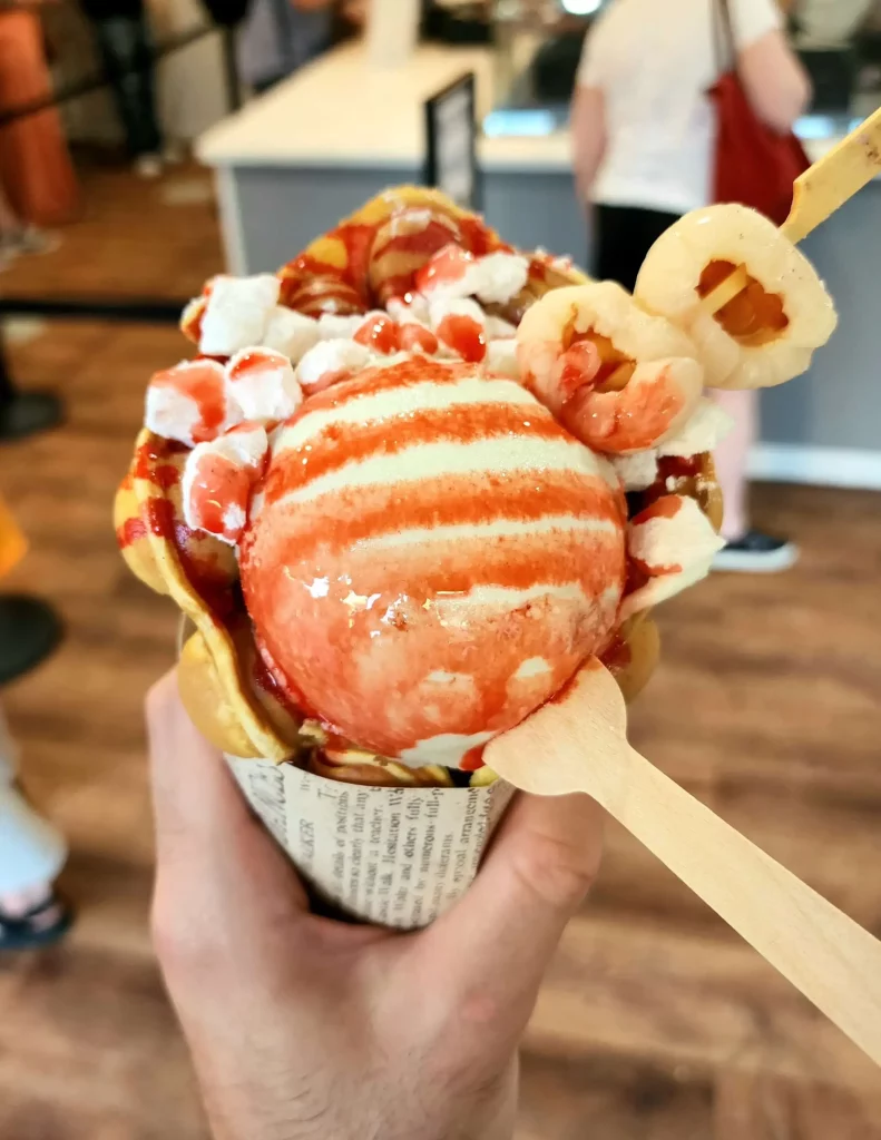 Close up: Pandan ice cream topped with lychee, mochi, and grenadine sauce, wrapped in a bubble waffle.