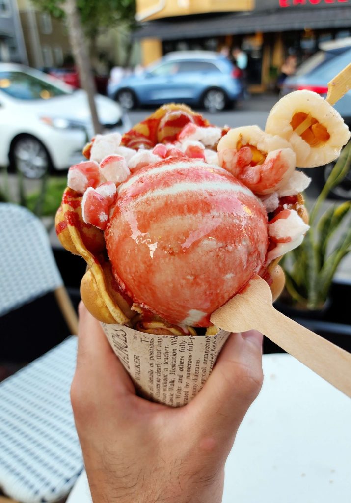 Close up: Pandan ice cream topped with lychee, mochi, and grenadine sauce, wrapped in a bubble waffle.