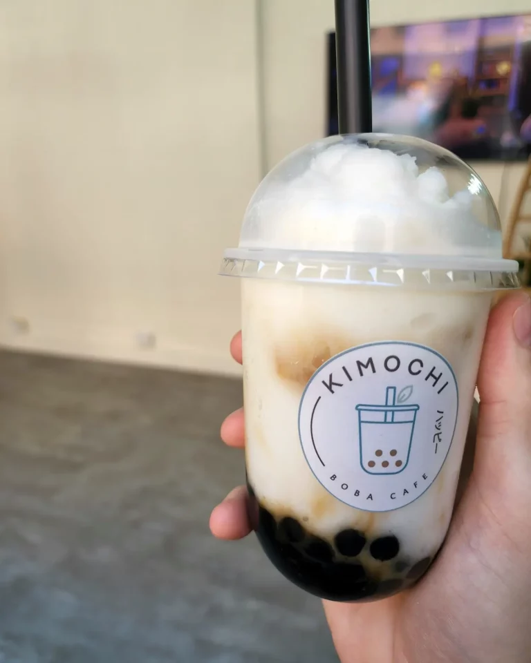 White and caramel color swirled bubble tea in a plastic cup with lid topped with whipped cream.