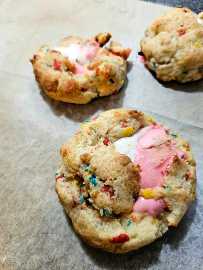 Fruity cereal cookie with marshmallow oozing out on a baking tray.