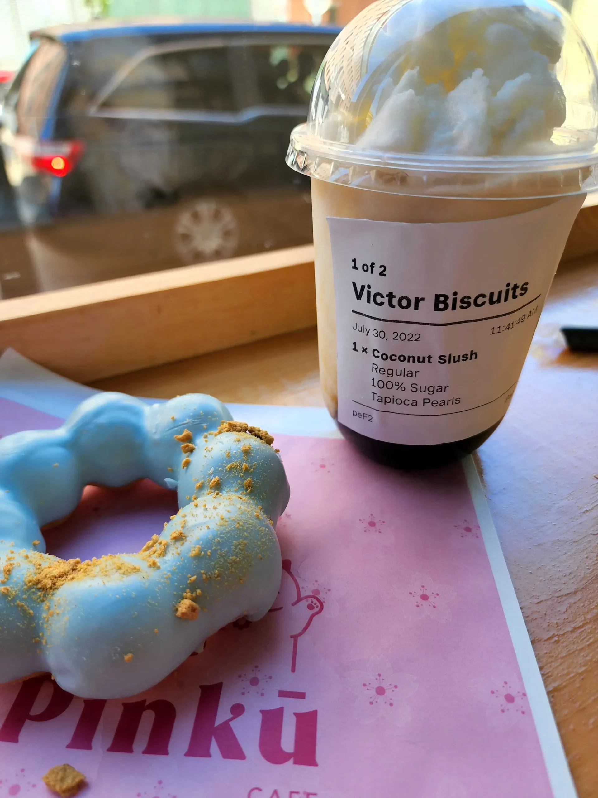 A light blue mochi donut next to a coconut slush boba tea on a counter in Kimochi Cafe.
