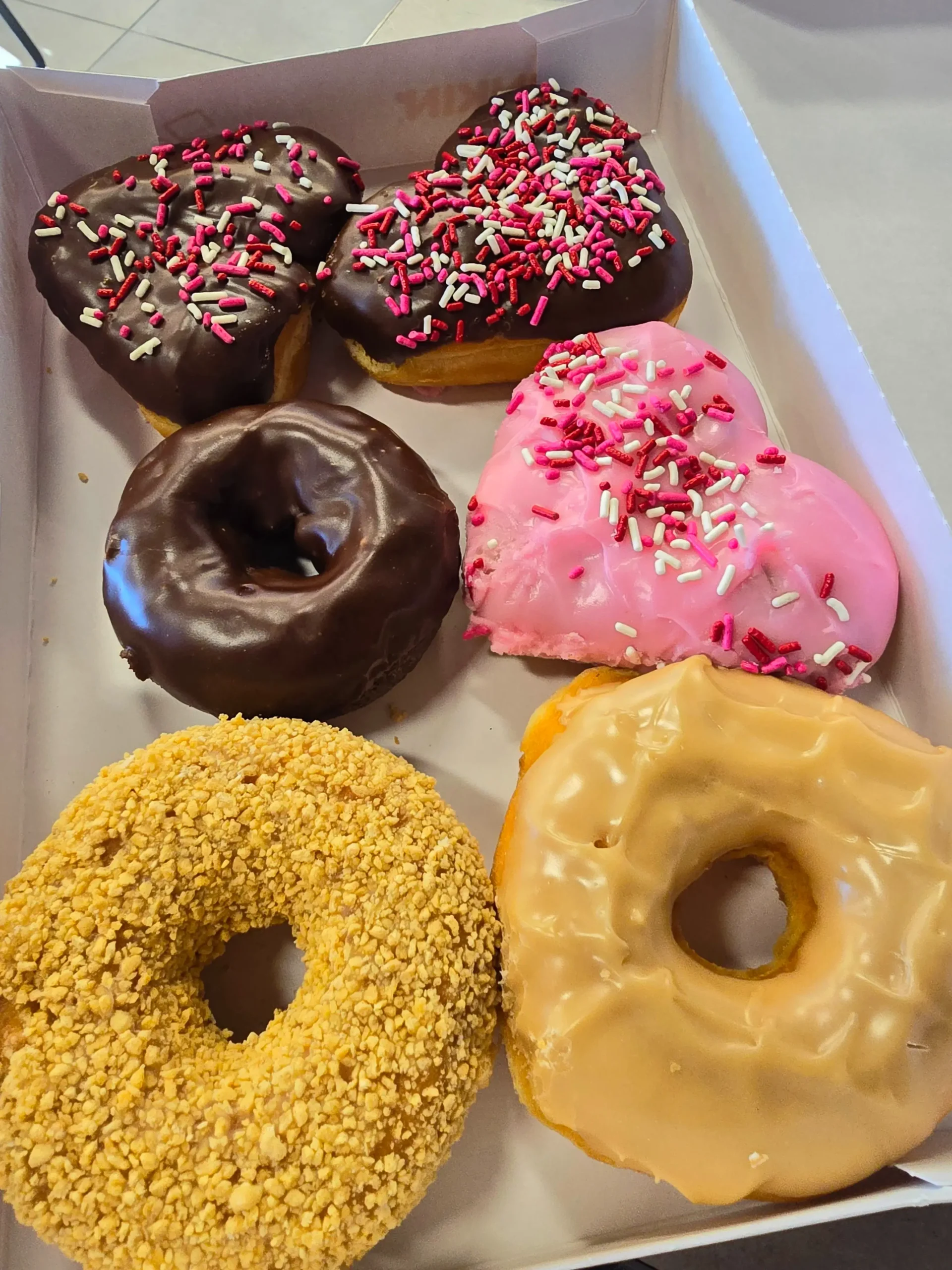 Box of Dunkin' Donuts Valentine's donuts including frosted strawberry Boston creme and chocolate frosted brownie batter heart.