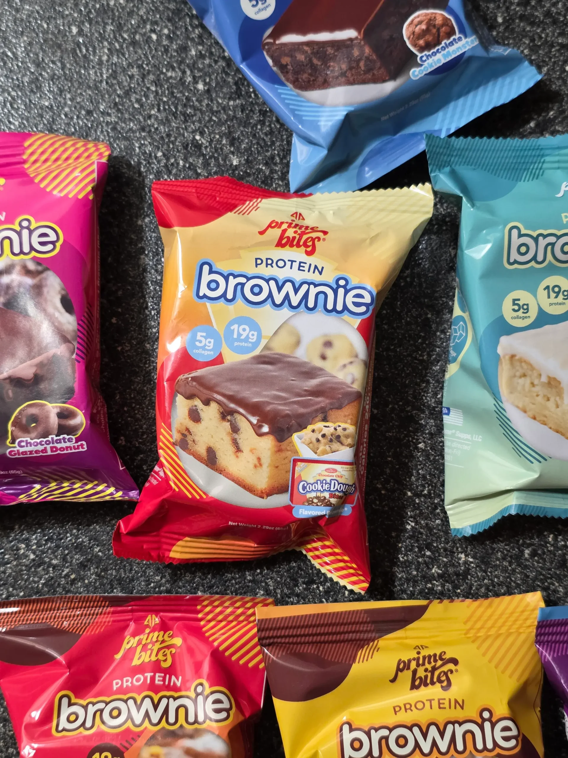 Prime Bites variety pack, including: Chocolate Glazed Donut, Glazed Cinnamon Roll, Birthday Cake, Banana Nut, Peanut Butter Candy Crunch, Chocolate Cookie Monster, Cookie Dough, Blueberry Cobbler, and Cookies & Cream Blondie.