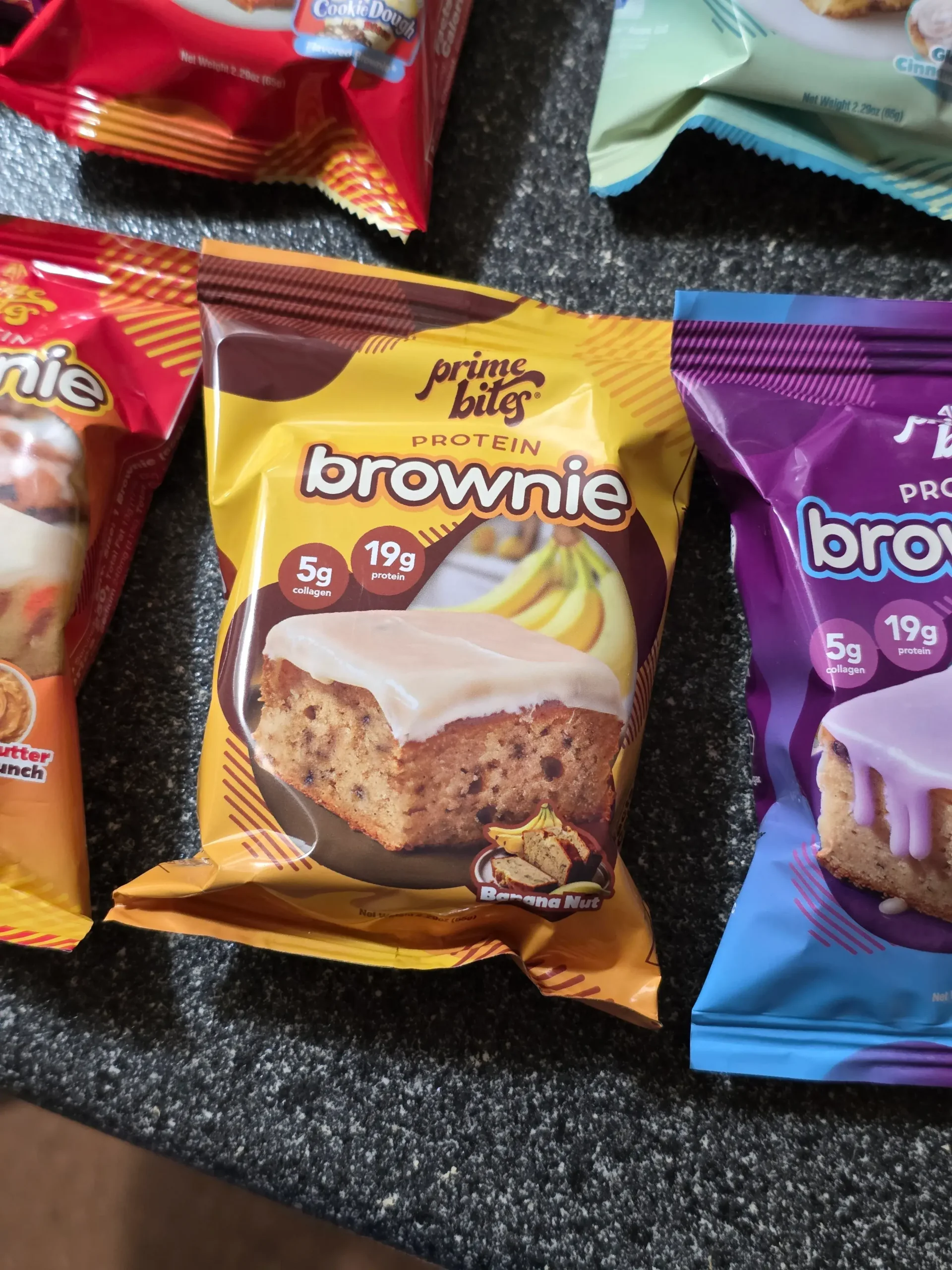 Prime Bites variety pack, including: Chocolate Glazed Donut, Glazed Cinnamon Roll, Birthday Cake, Banana Nut, Peanut Butter Candy Crunch, Chocolate Cookie Monster, Cookie Dough, Blueberry Cobbler, and Cookies & Cream Blondie.