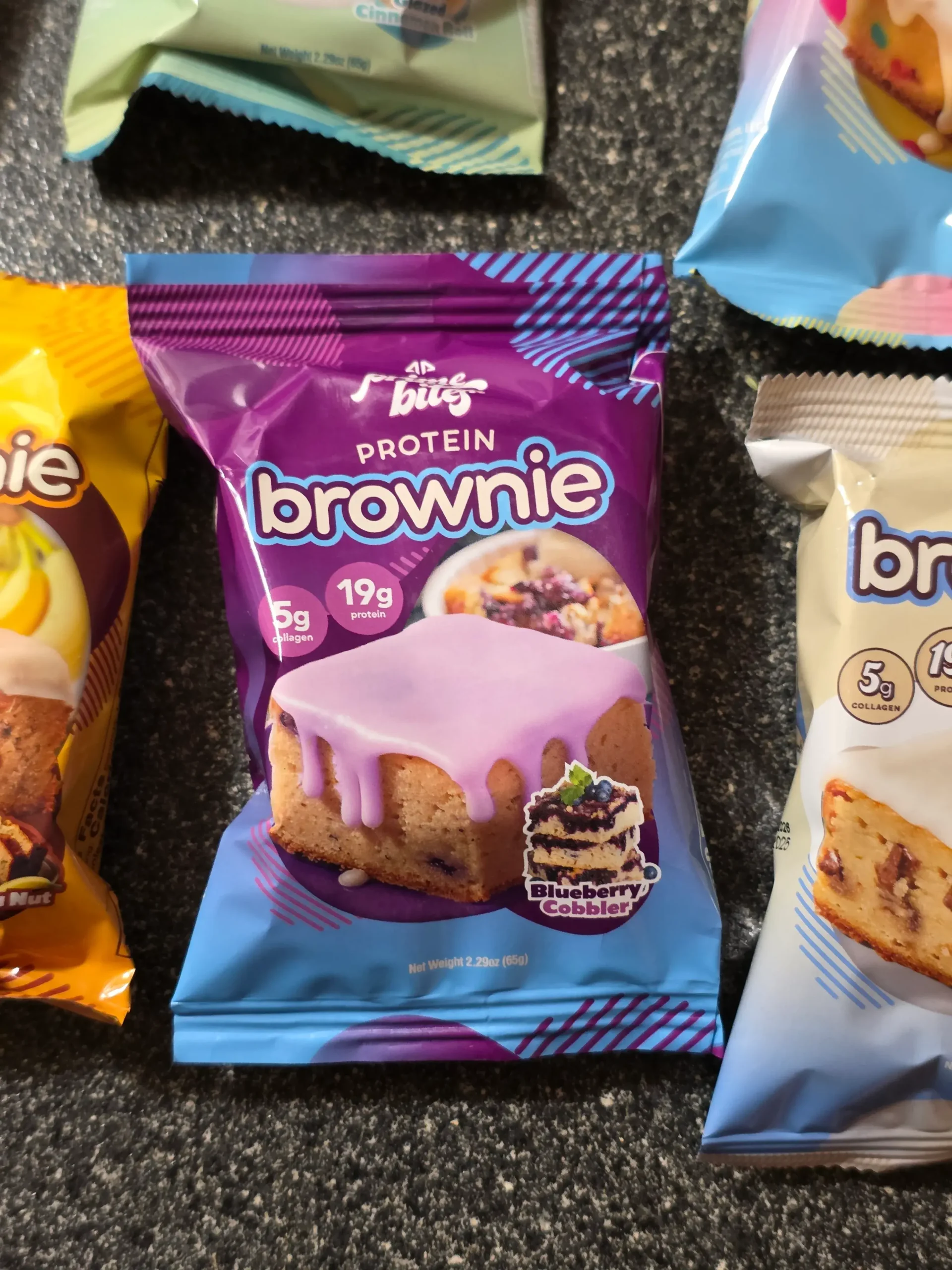 Prime Bites variety pack, including: Chocolate Glazed Donut, Glazed Cinnamon Roll, Birthday Cake, Banana Nut, Peanut Butter Candy Crunch, Chocolate Cookie Monster, Cookie Dough, Blueberry Cobbler, and Cookies & Cream Blondie.