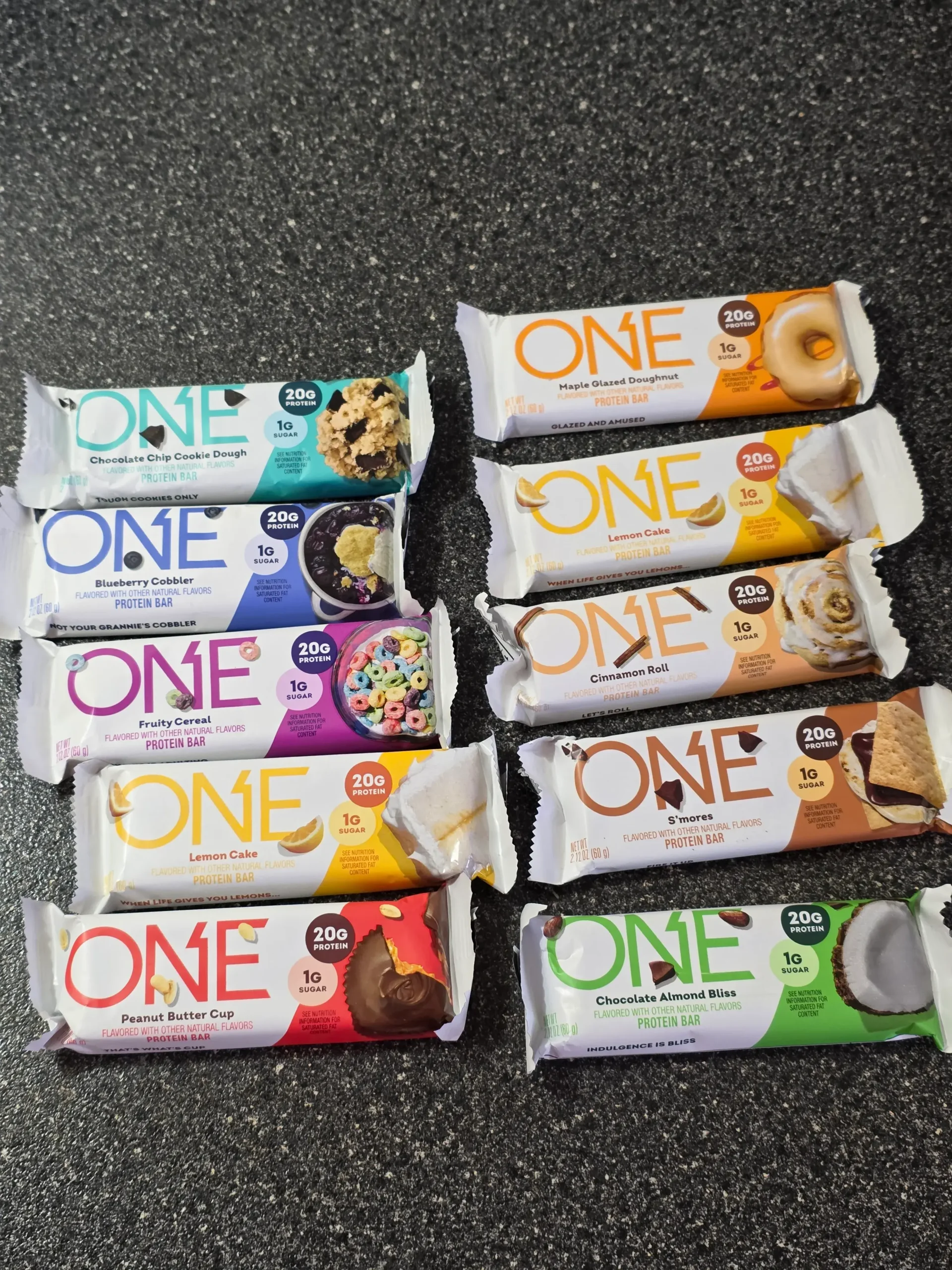 ONE Protein Bar Variety Sample Pack: Maple Glazed Doughnut, Lemon Cake, Cinnamon Roll, S'mores, Chocolate Almond Bliss, Chocolate Chip Cookie Dough, Blueberry Cobbler, Fruity Cereal, Lemon Cake, and Peanut Butter Cup.