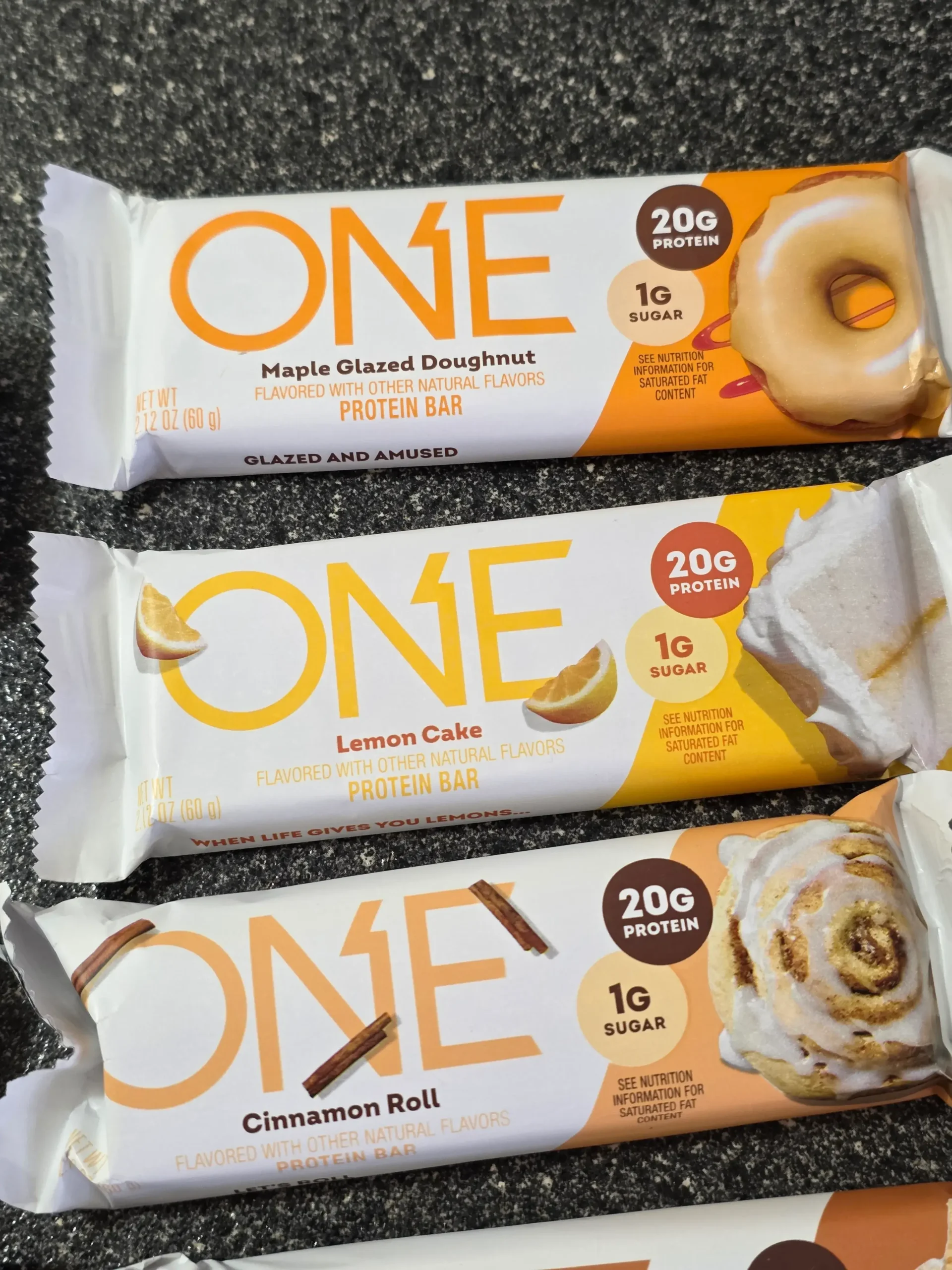 ONE Protein Bar Variety Sample Pack: Maple Glazed Doughnut, Lemon Cake, Cinnamon Roll, S'mores, Chocolate Almond Bliss, Chocolate Chip Cookie Dough, Blueberry Cobbler, Fruity Cereal, Lemon Cake, and Peanut Butter Cup.
