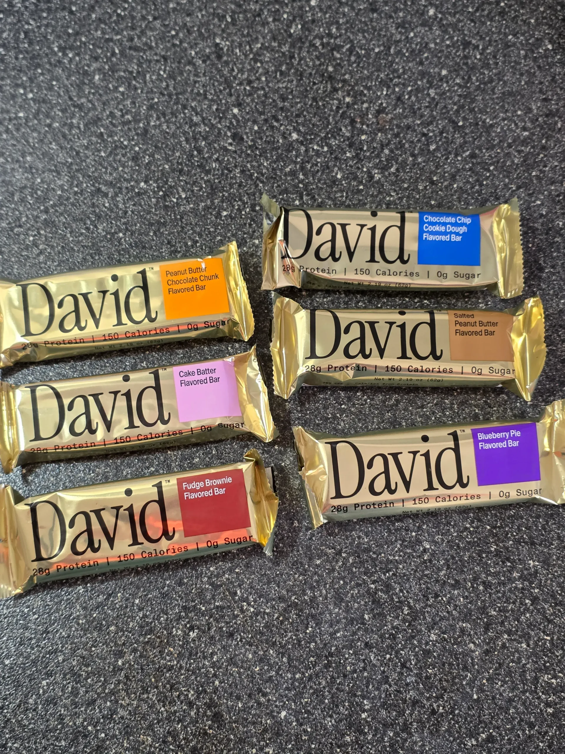 David Protein Bar: Cinnamon Roll, Red Velvet, Fudge Brownie, Cake Batter, Peanut Butter Chocolate Chunk,  Chocolate Chip Cookie Dough, Salted Peanut Butter, and Blueberry Pie.