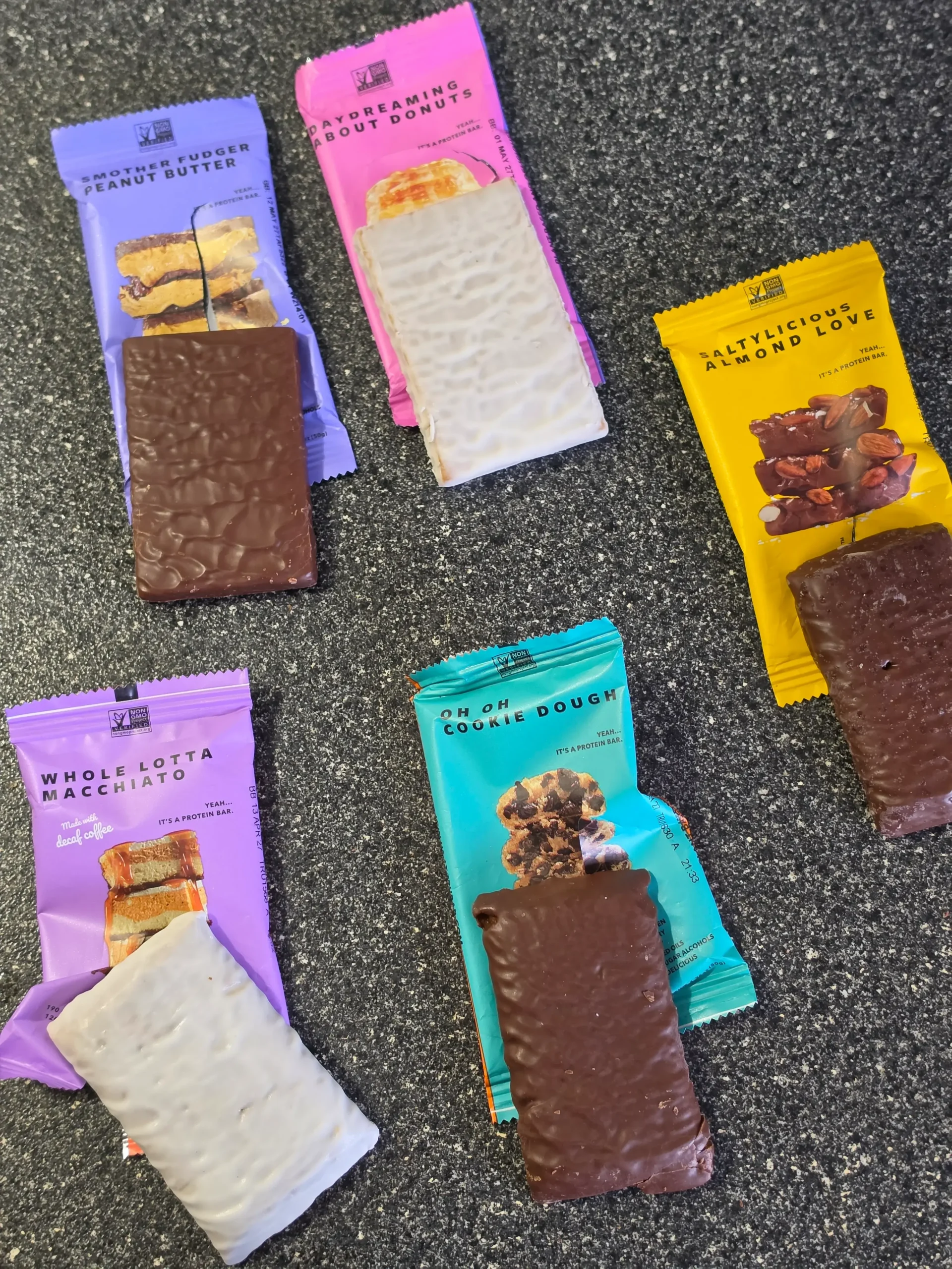 TRUBAR plant-based protein bars, including flavors Daydreaming About Donuts, Smother Fudger Peanut Butter, Saltylicious Almond Love, Whole Lotta Macchiato, and Oh Oh Cookie Dough.