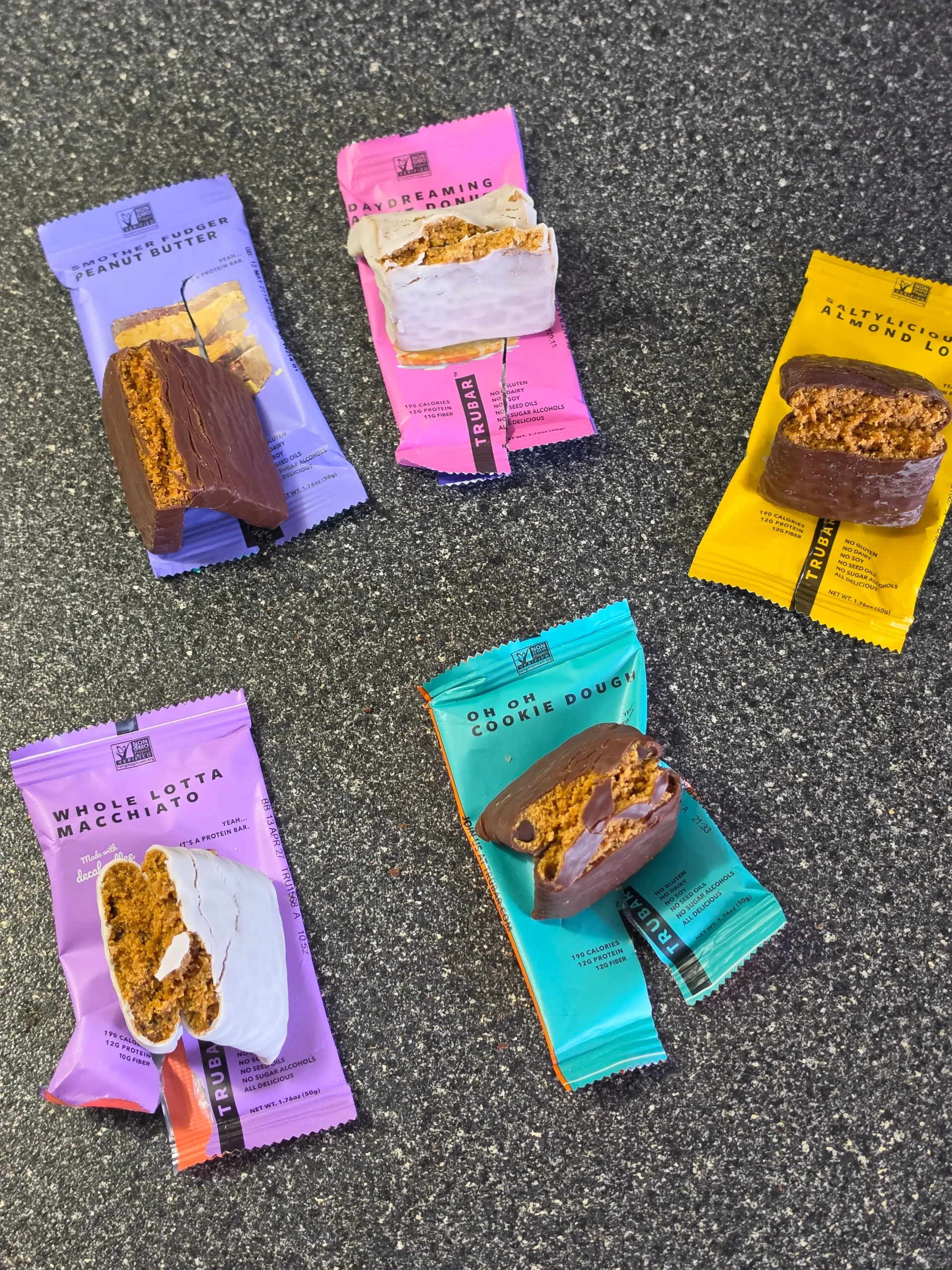 TRUBAR plant-based protein bars, including flavors Daydreaming About Donuts, Smother Fudger Peanut Butter, Saltylicious Almond Love, Whole Lotta Macchiato, and Oh Oh Cookie Dough.